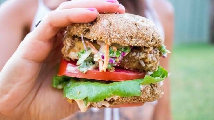 A grass-fed beef sandwich piled with slaw, tomato and lettuce on a whole-grain bun